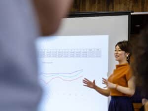 A woman presents to a room with a big screen