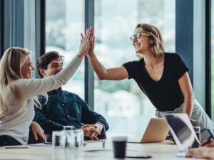 Female professional giving a high five to her colleague in conference room. Group of colleagues celebrating success in a meeting