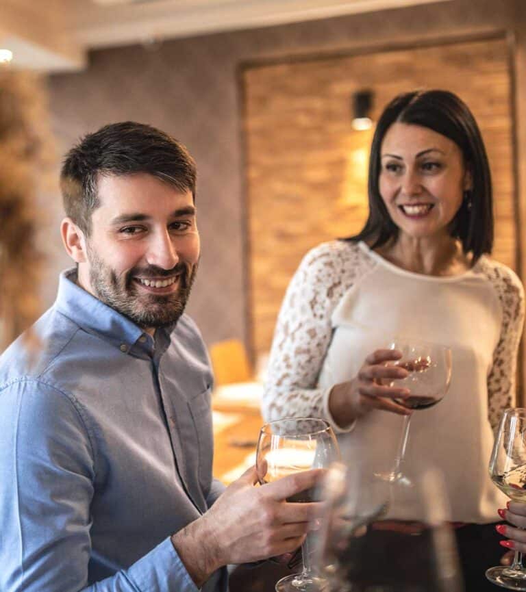 A male and female pair of colleagues sip wine at a work event