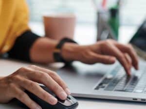 A close up of a person using her mouse and laptop at a desk