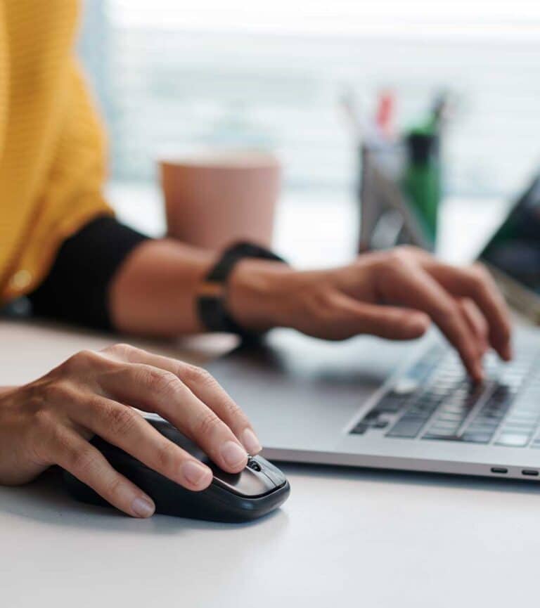 A close up of a person using her mouse and laptop at a desk