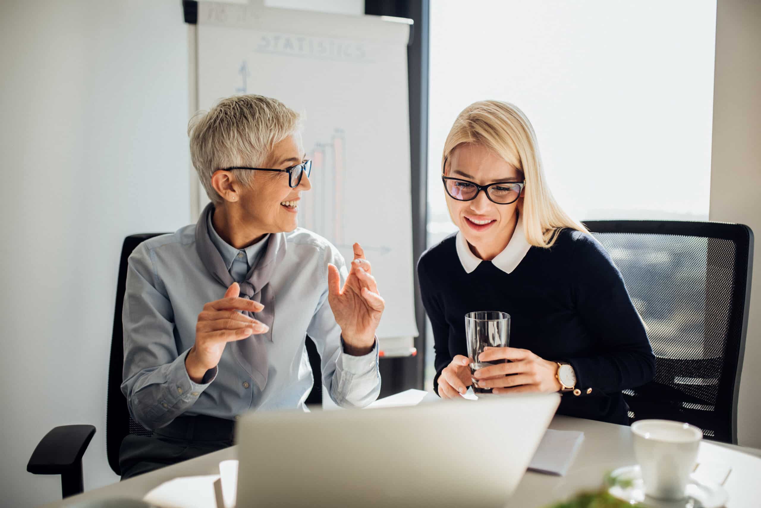 Young business woman looking at laptop when listening to mature coworker