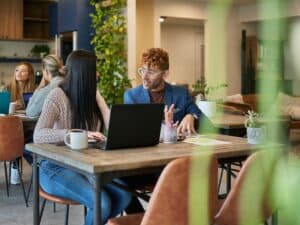 Groups of young men and women sitting at tables in coworking office environment and discussing small business plans and projects.
