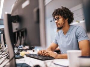 Young black computer programmer coding software while working on PC in the office.