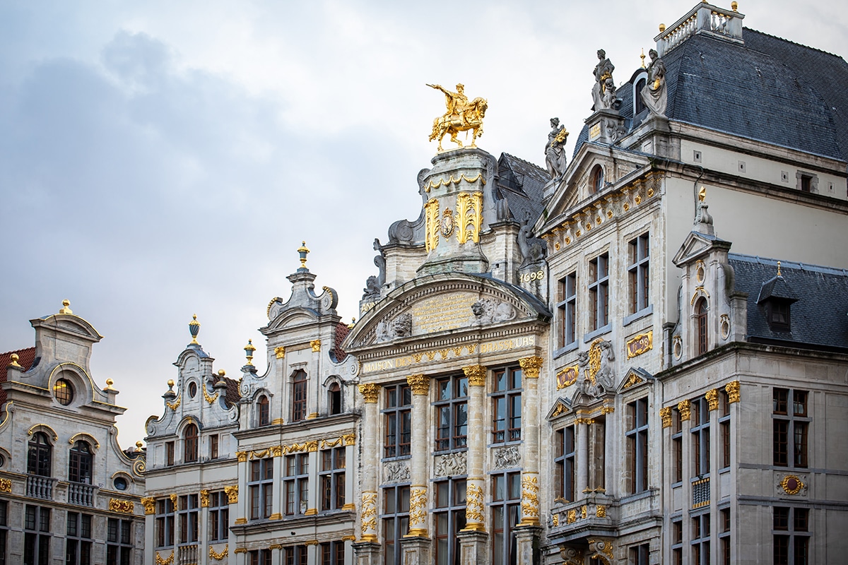 Ornate historic buildings in Grand Place, Brussels, featuring gold-accented facades, statues, and the Maison des Brasseurs building with a golden horse and rider statue.