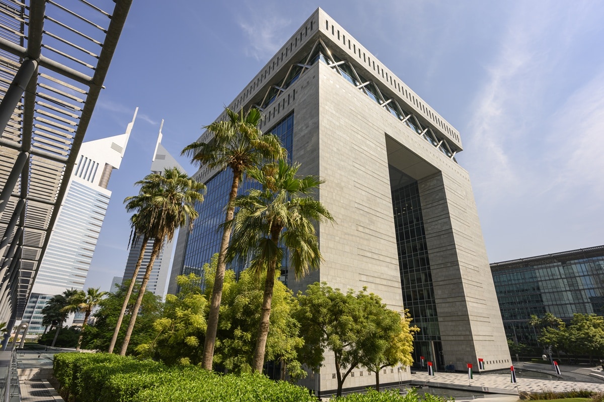 Dubai International Financial Centre Gate Building rising against a clear sky, showcasing modern architecture with palm trees and lush greenery in a prime business district