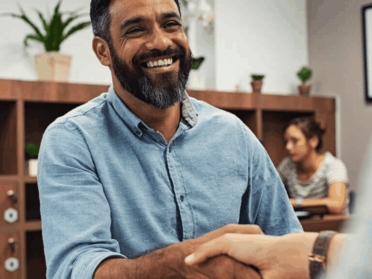 A gentleman in a blue shirt smiles whilst shaking someone's hand