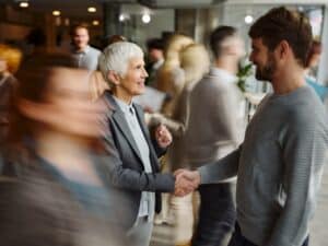 Happy entrepreneurs shaking hands after meeting in a hallway among people in blurred motion.