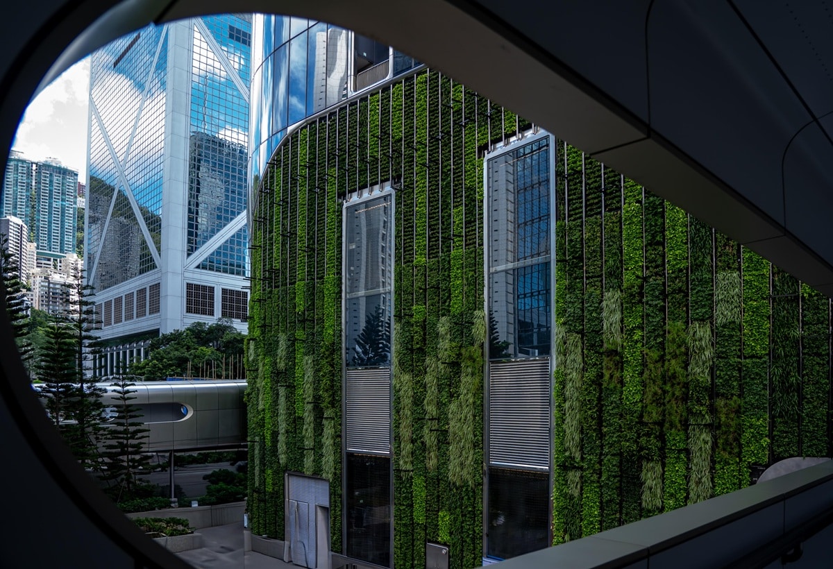 A modern building in Hong Kong with a vertical green wall and windows that reflect the city's skyline.