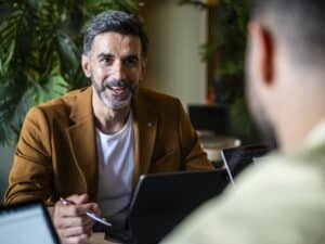 Business professional in his 30s holding pen and looking towards co-worker, explaining, ideas, innovation