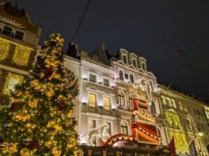 London, UK - December 29 2025: A decorated Christmas tree stands before the Cartier flagship store on New Bond Street, featuring a large glowing panther and gift box light display in Mayfair