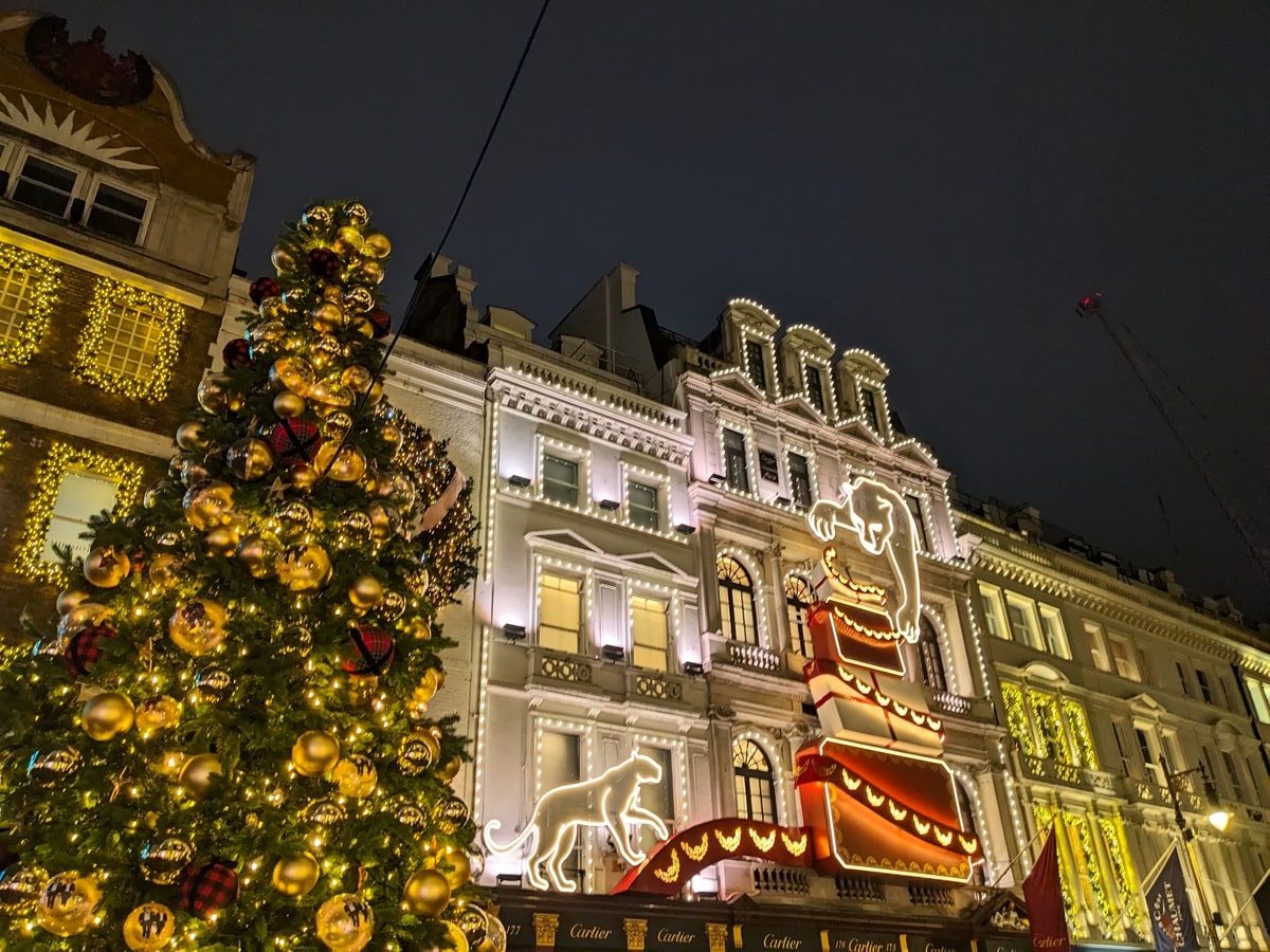 London, UK - December 29 2025: A decorated Christmas tree stands before the Cartier flagship store on New Bond Street, featuring a large glowing panther and gift box light display in Mayfair